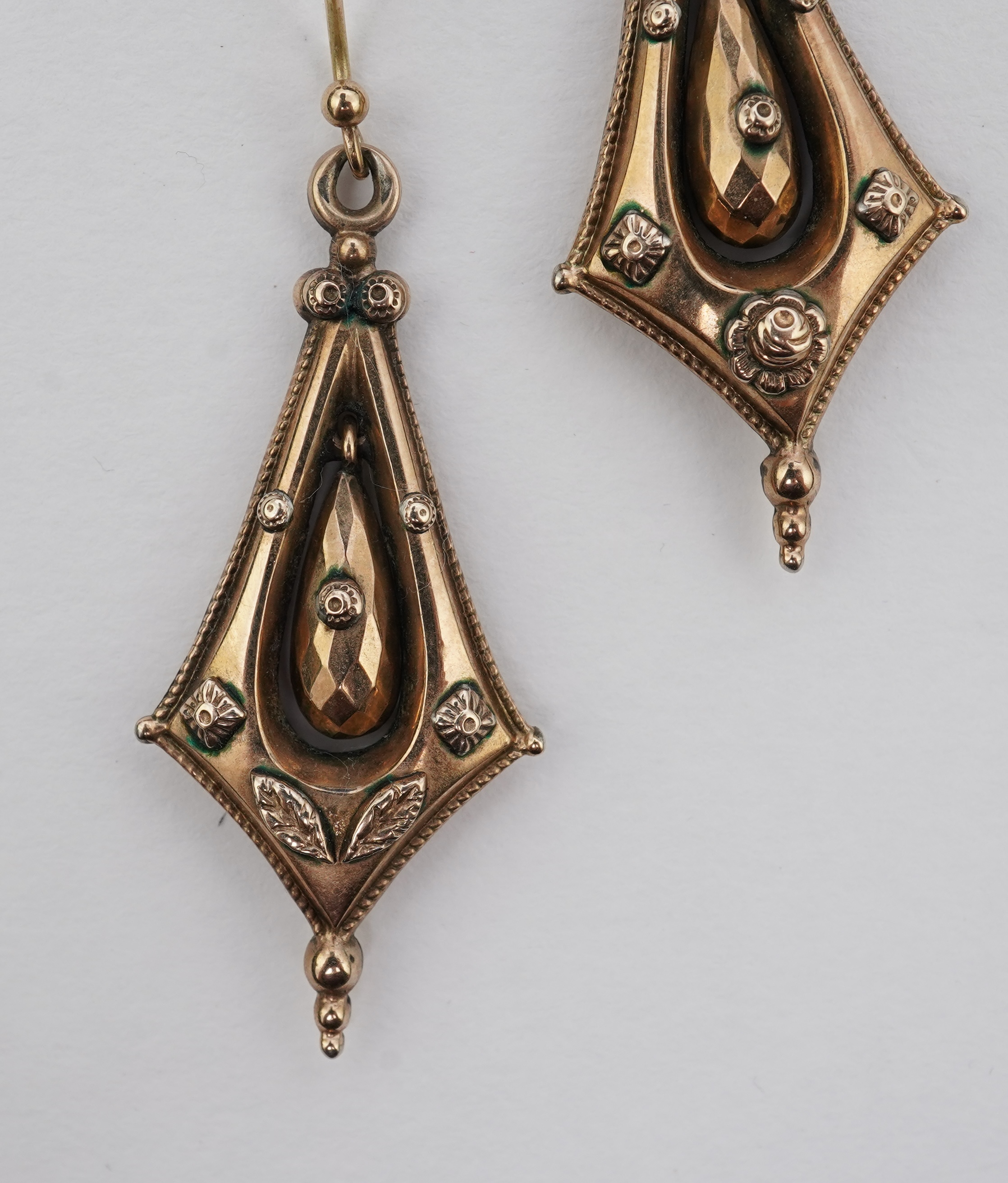 A pair of Victorian gold earrings, late 19th century, each of drop design, outlined with a rope twist border and accented with floral and foliate motifs, the centres suspending faceted pendants, length 5.8cm, one slightl